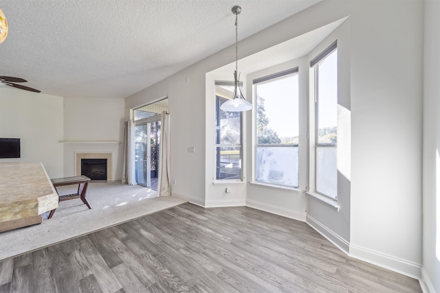 unfurnished living room featuring baseboards, ceiling fan, a tile fireplace, wood finished floors, and a textured ceiling