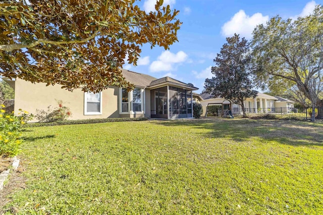 rear view of property featuring a yard, fence, a sunroom, and stucco siding