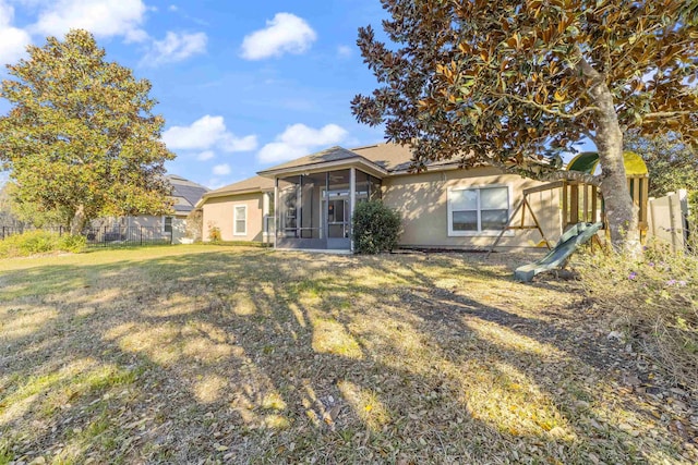 rear view of property featuring stucco siding, a lawn, fence, and a sunroom