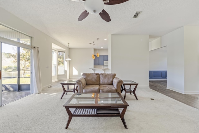 carpeted living room with baseboards, visible vents, a textured ceiling, and a ceiling fan