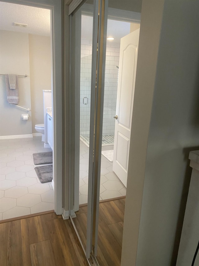 hall featuring visible vents, baseboards, a textured ceiling, and wood finished floors