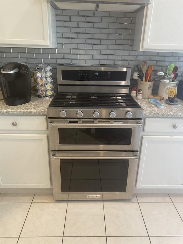 kitchen with decorative backsplash, white cabinets, light tile patterned flooring, and double oven range