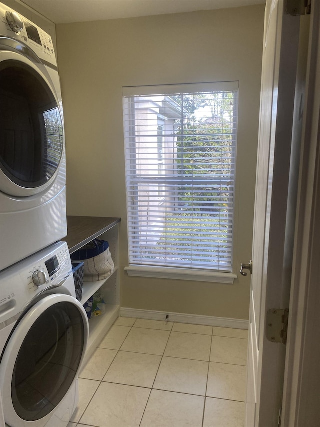 clothes washing area with light tile patterned floors, stacked washer / drying machine, baseboards, and laundry area