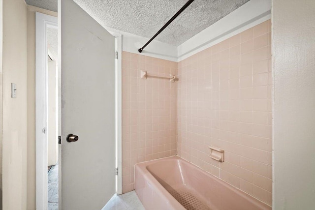 bathroom featuring a textured ceiling and tiled shower / bath