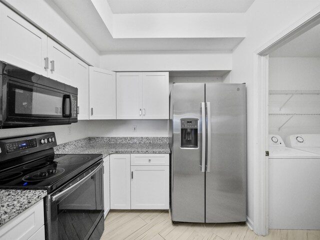 kitchen with white cabinetry, light stone counters, light hardwood / wood-style floors, black appliances, and washer and dryer