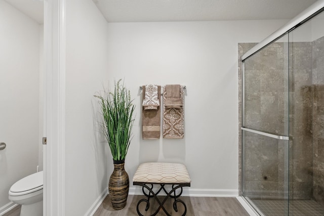 full bathroom with a shower stall, wood finished floors, toilet, and baseboards