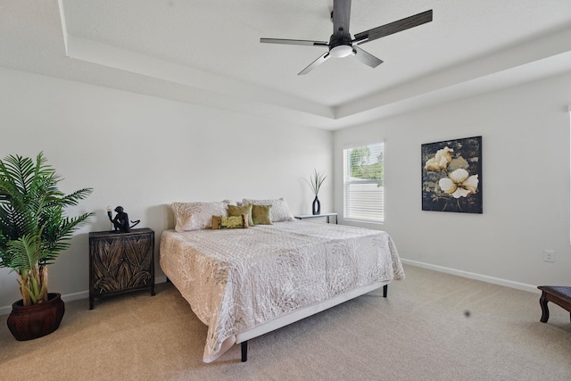 bedroom with light carpet, a tray ceiling, baseboards, and a ceiling fan