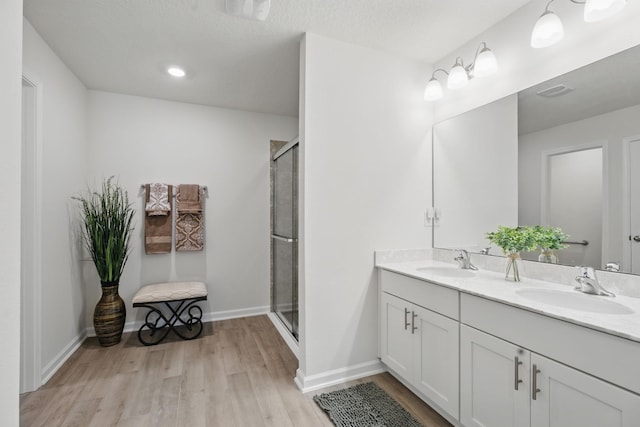 full bathroom with wood finished floors, a shower stall, double vanity, and baseboards