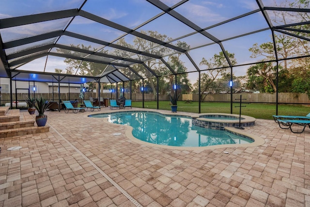 pool at dusk featuring a lanai, an in ground hot tub, a yard, and a patio