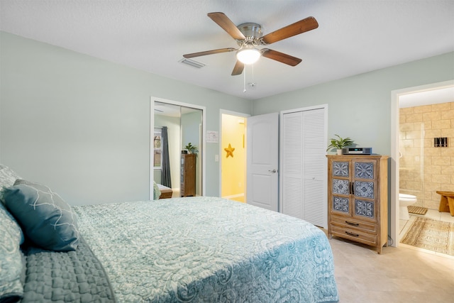 bedroom with two closets, ensuite bathroom, ceiling fan, and tile walls