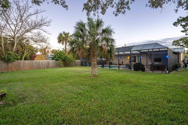 yard at dusk featuring glass enclosure and a swimming pool