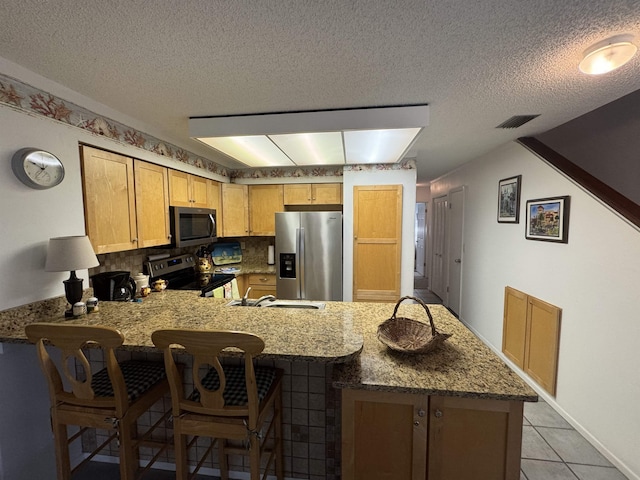59 Village Del Lago Cir Unit 59, Saint Augustine, FL 32080 - kitchen featuring appliances with stainless steel finishes, a peninsula, light stone countertops, a textured ceiling, and a breakfast bar area