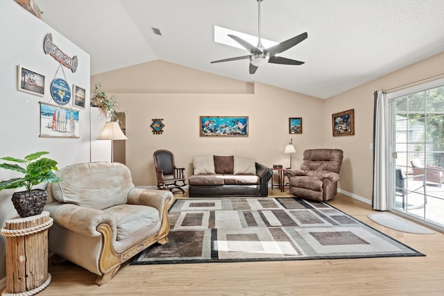 living room featuring hardwood / wood-style floors, lofted ceiling with skylight, and ceiling fan