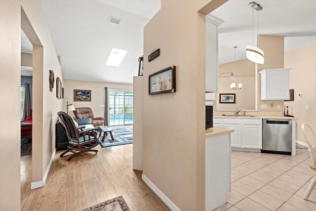 corridor with a chandelier, light hardwood / wood-style floors, lofted ceiling with skylight, and sink