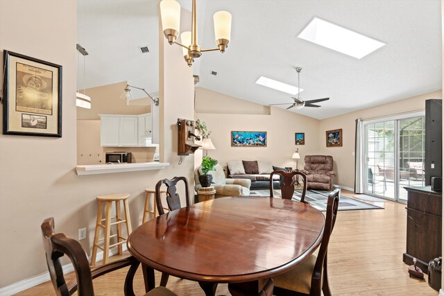 dining area featuring lofted ceiling with skylight, ceiling fan with notable chandelier, and light wood-type flooring