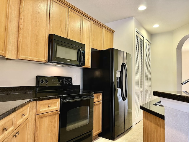 kitchen featuring black appliances, light tile patterned floors, and dark stone counters