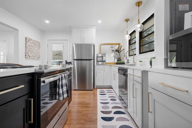 kitchen featuring appliances with stainless steel finishes, light wood-type flooring, sink, decorative light fixtures, and white cabinetry