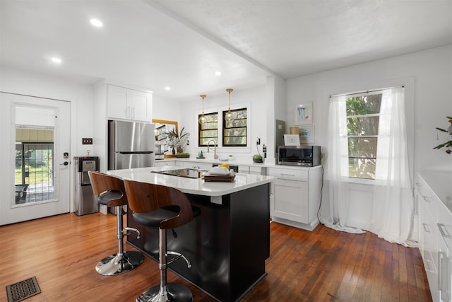 kitchen with a healthy amount of sunlight, a kitchen island, white cabinetry, and appliances with stainless steel finishes