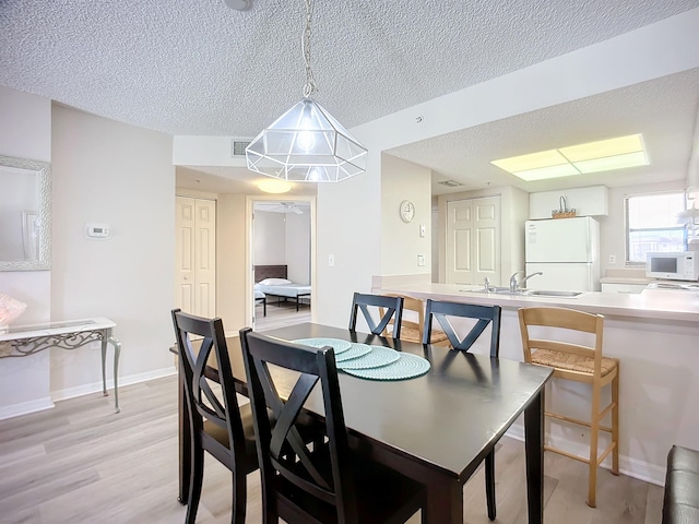 dining space with a textured ceiling, light wood-type flooring, and sink