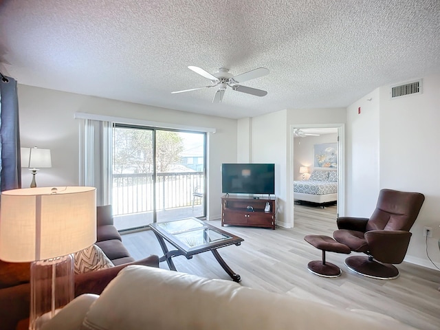 living room featuring ceiling fan, a textured ceiling, and light wood-type flooring