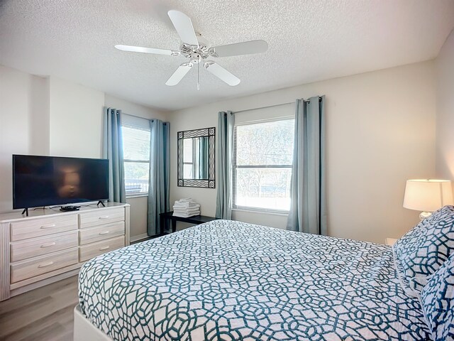 bedroom with multiple windows, ceiling fan, a textured ceiling, and hardwood / wood-style flooring