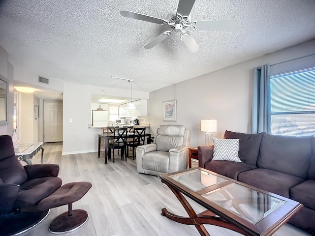 living room with a textured ceiling, light hardwood / wood-style floors, and ceiling fan