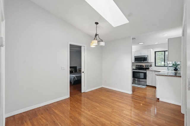 131 Boulder Rock Dr, Palm Coast, FL 32137 - kitchen with appliances with stainless steel finishes, a skylight, light wood-style flooring, white cabinets, and decorative light fixtures