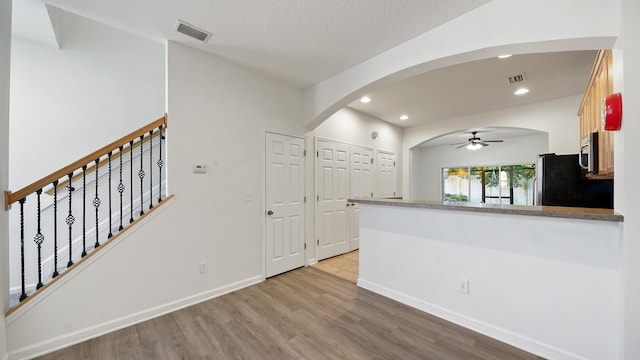 kitchen with ceiling fan, light hardwood / wood-style flooring, kitchen peninsula, refrigerator, and a textured ceiling