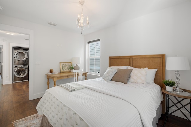 bedroom featuring a notable chandelier, dark wood-type flooring, and stacked washer and clothes dryer