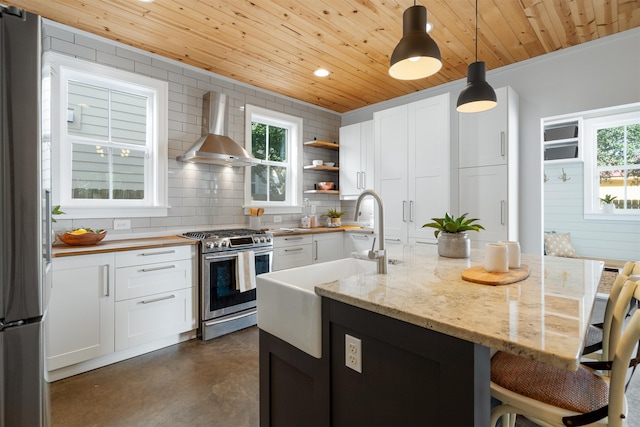 kitchen featuring decorative light fixtures, wall chimney exhaust hood, plenty of natural light, white cabinetry, and stainless steel appliances