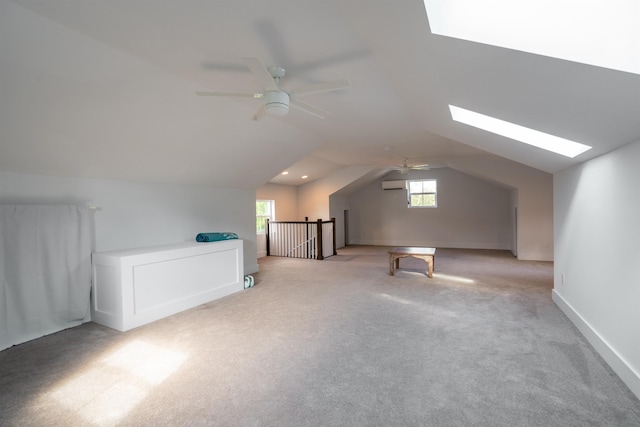 additional living space with light colored carpet, lofted ceiling with skylight, ceiling fan, and an AC wall unit