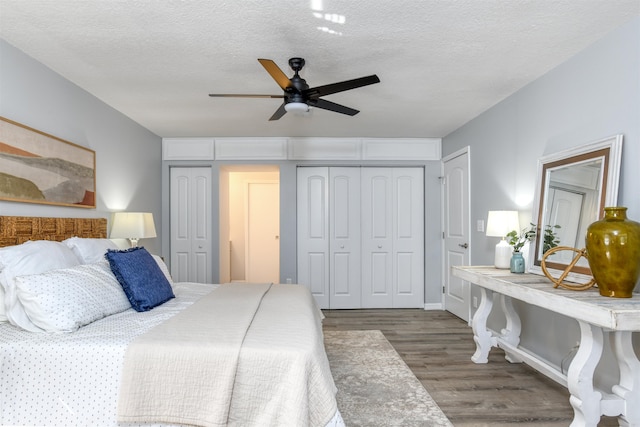 bedroom with multiple closets, a textured ceiling, ceiling fan, and dark wood-type flooring