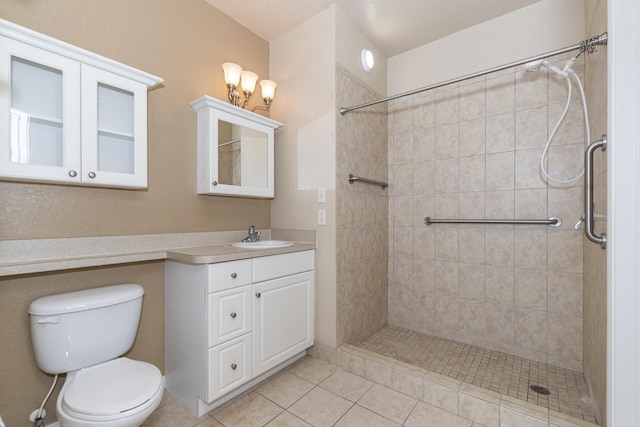 bathroom featuring vanity, a tile shower, tile patterned floors, and toilet