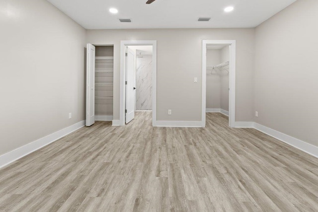 unfurnished bedroom with a spacious closet, visible vents, baseboards, and light wood-style flooring