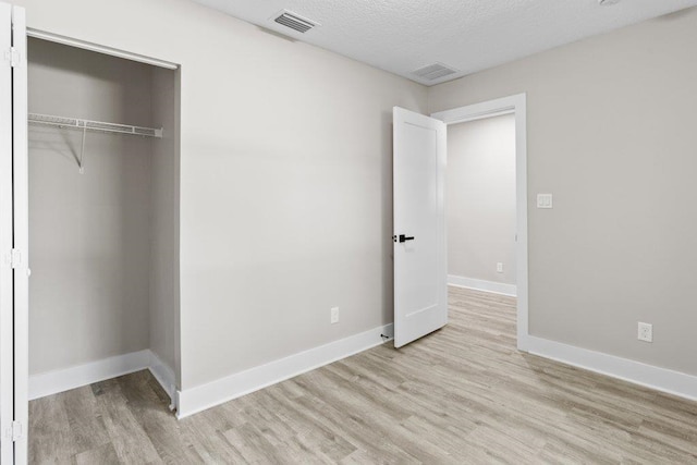 unfurnished bedroom featuring wood finished floors, visible vents, a closet, and baseboards