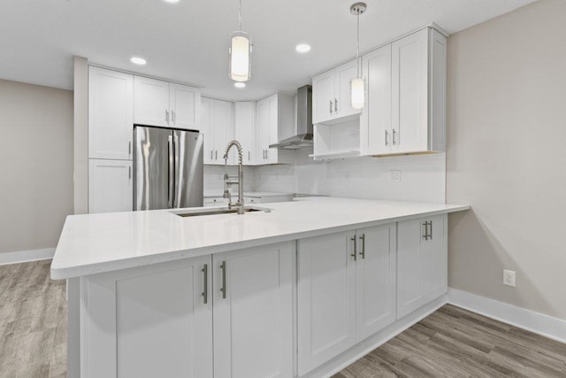 kitchen with freestanding refrigerator, wall chimney exhaust hood, a peninsula, a sink, and baseboards