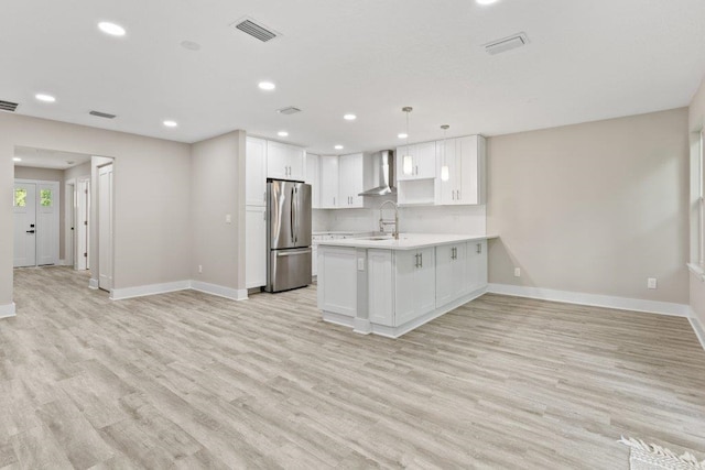 kitchen featuring wall chimney range hood, visible vents, baseboards, and freestanding refrigerator