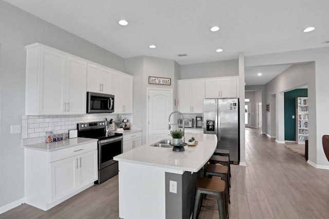 123 Hickory Ridge Rd, Saint Augustine, FL 32084 - kitchen featuring appliances with stainless steel finishes, a kitchen island with sink, a kitchen breakfast bar, backsplash, and light wood finished floors