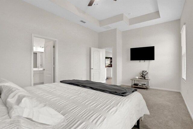 carpeted bedroom with ceiling fan, a raised ceiling, and ensuite bathroom