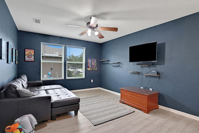 living room featuring ceiling fan, light hardwood / wood-style floors, and a textured ceiling