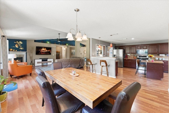 14 Serbian Bellflower Trl, Palm Coast, FL 32164 - dining space with light wood finished floors, ceiling fan with notable chandelier, a lit fireplace, and lofted ceiling
