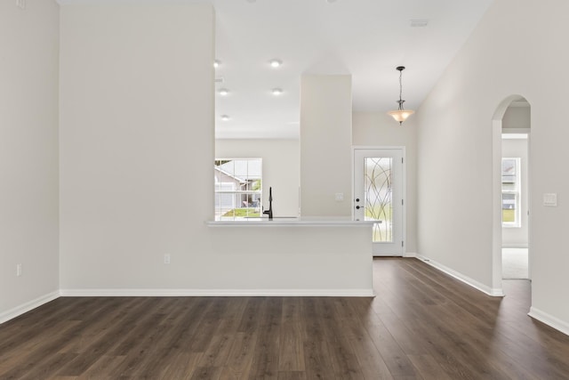 foyer entrance featuring arched walkways, dark wood-type flooring, and baseboards