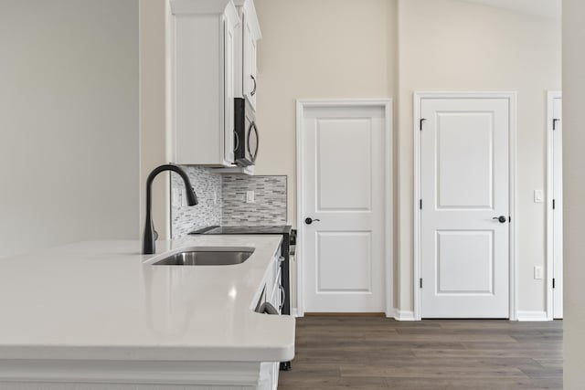 kitchen featuring dark wood-style floors, a sink, white cabinets, stainless steel microwave, and tasteful backsplash