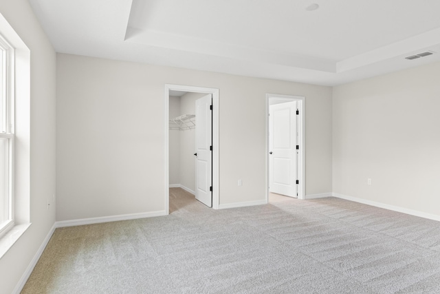 empty room featuring light carpet, visible vents, a raised ceiling, and baseboards