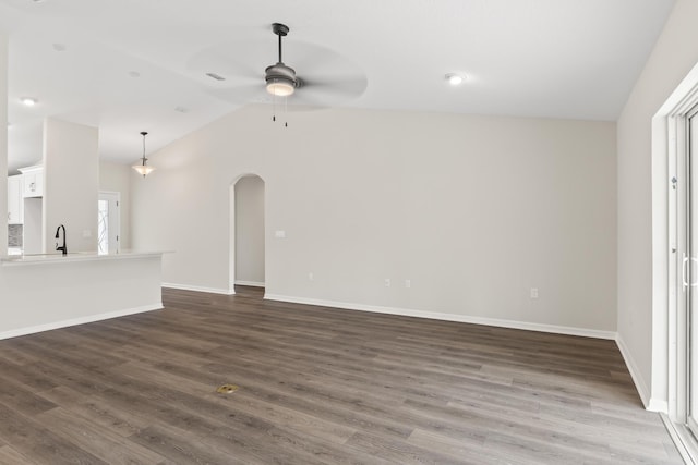 unfurnished living room with ceiling fan, dark wood finished floors, vaulted ceiling, arched walkways, and a sink