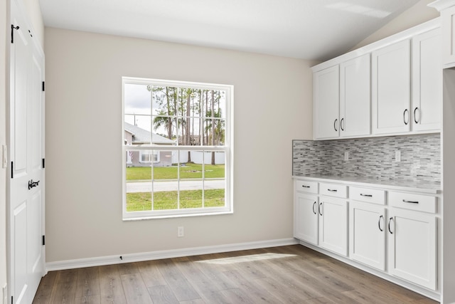 interior space with light wood-type flooring, backsplash, white cabinets, light countertops, and baseboards