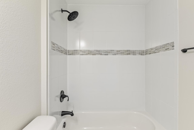 bathroom featuring toilet, shower / bathing tub combination, and a textured wall