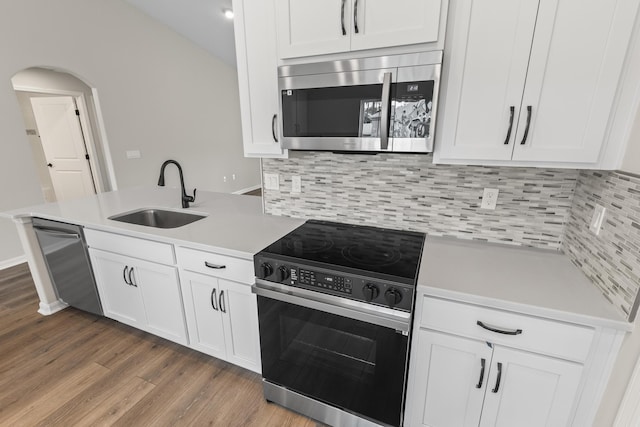 kitchen with wood finished floors, arched walkways, a sink, light countertops, and appliances with stainless steel finishes