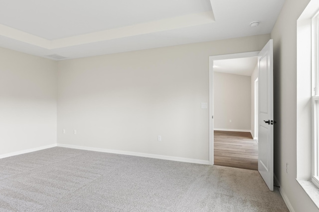 spare room featuring a raised ceiling, baseboards, and carpet floors