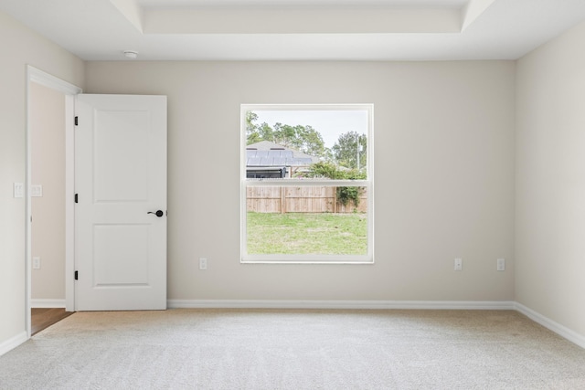 carpeted spare room featuring baseboards and a tray ceiling